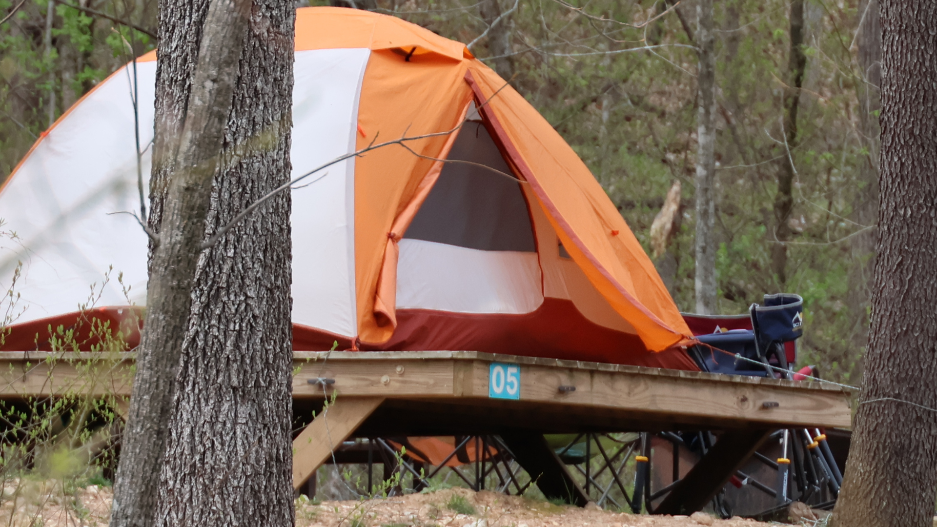 Orange camping tent on a wooden platform in the woods