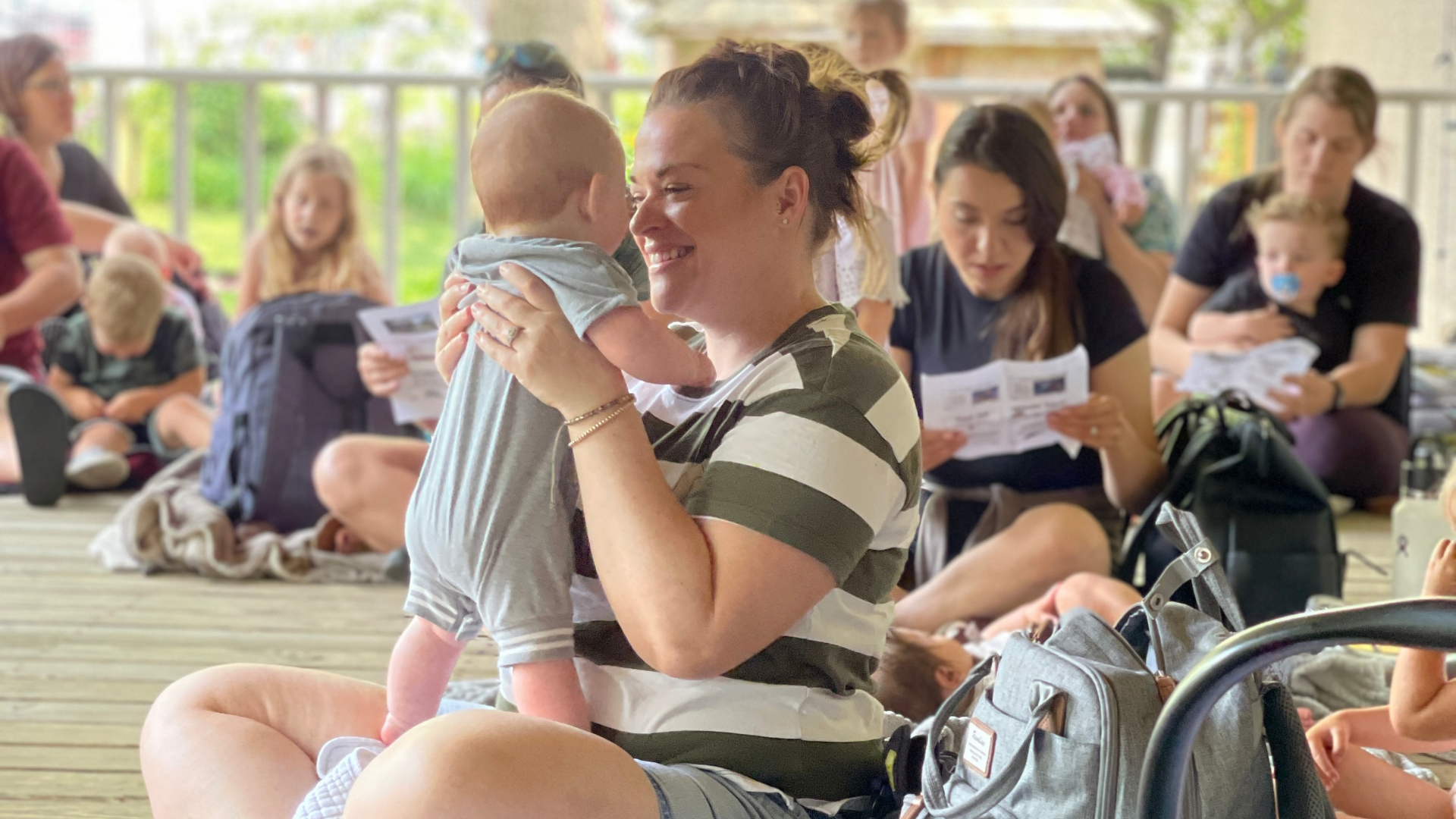 A mother holds her baby face to face, smiling while enjoying songs during Story Time at Peel Museum on the porch
