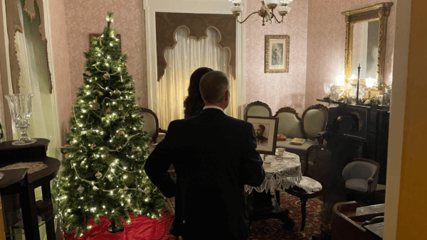 A photo of nicely dressed tour goers admiring the pink parlor at Peel Museum decorated for Christmas