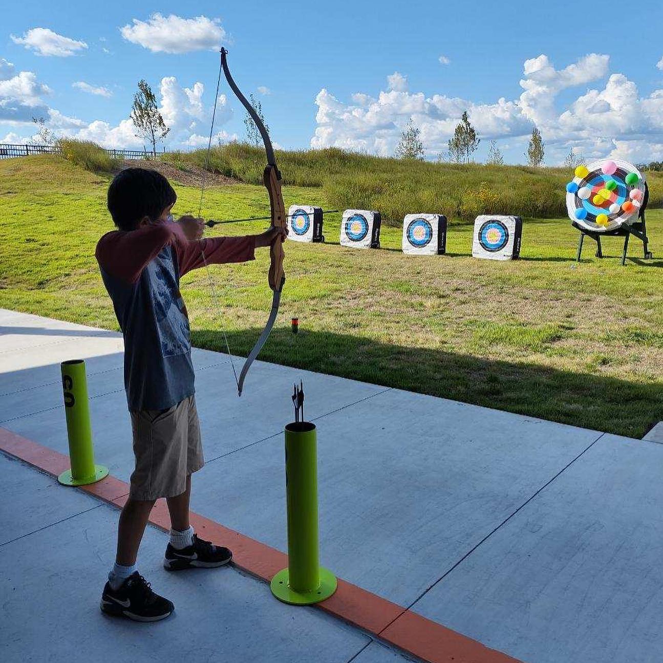 A photo of a boy aiming at a target of balloons with a bow and arrow at The Quiver Archery Range
