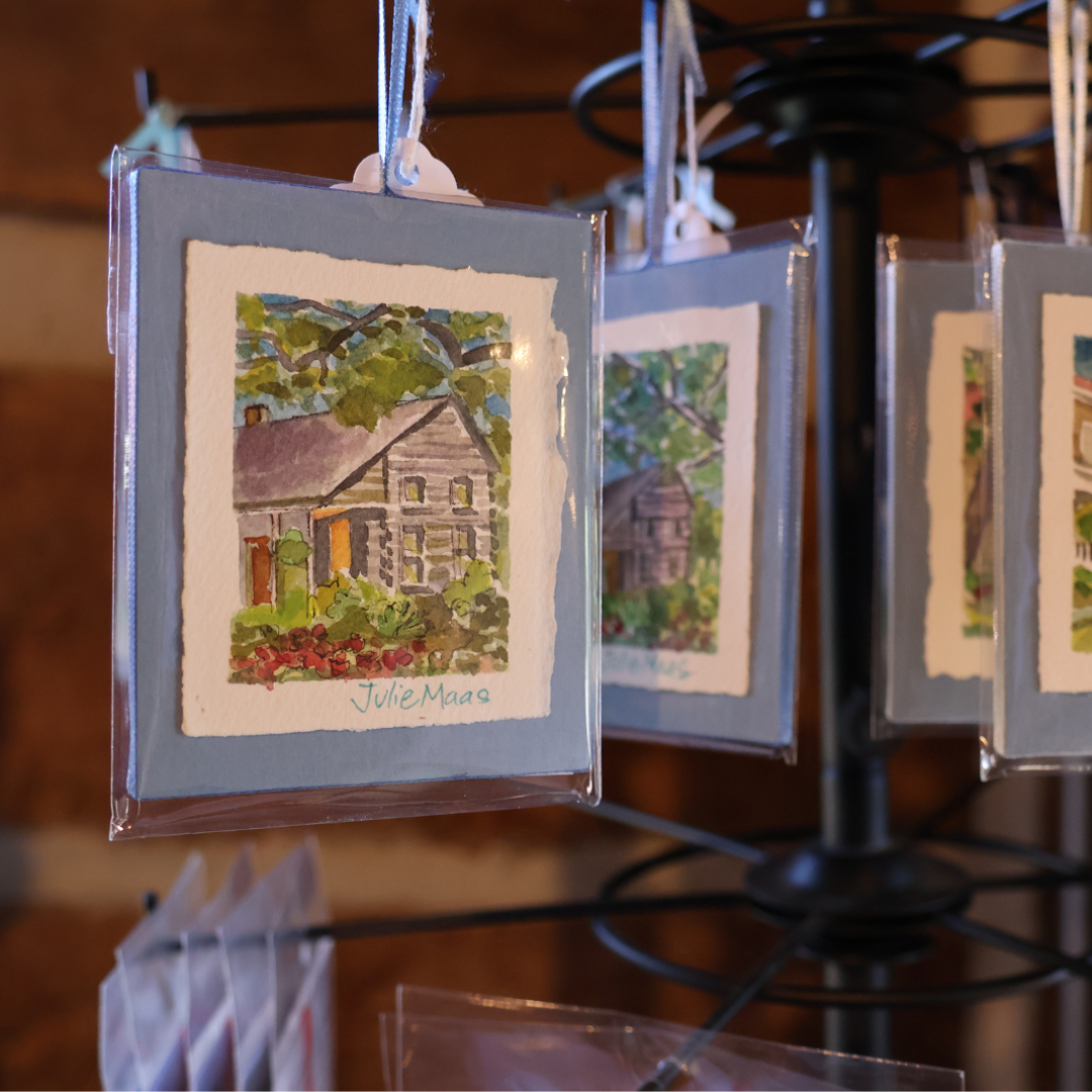 Mini Original Watercolor Paintings By Julie Maas a Local Bentonville Arkansas Artist - there are several mini paintings hanging from a rack with light blue ribbon at Museum Store