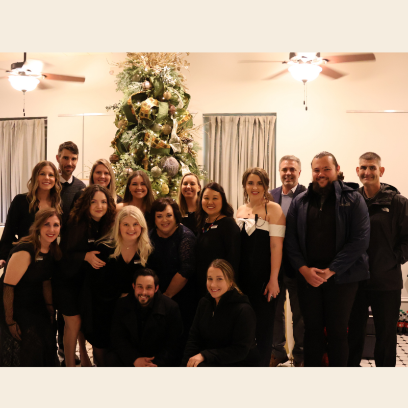 Peel Compton Foundation Team Photo at Christmas Event - Team is dressed in black and everyone is standing in front of Christmas Tree Smiling