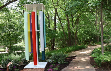 Photo of art installation at Compton Gardens - "Untitled (Wind Chimes) | 2014-2021." Features colorful, powder-coated aluminum and steel chimes.