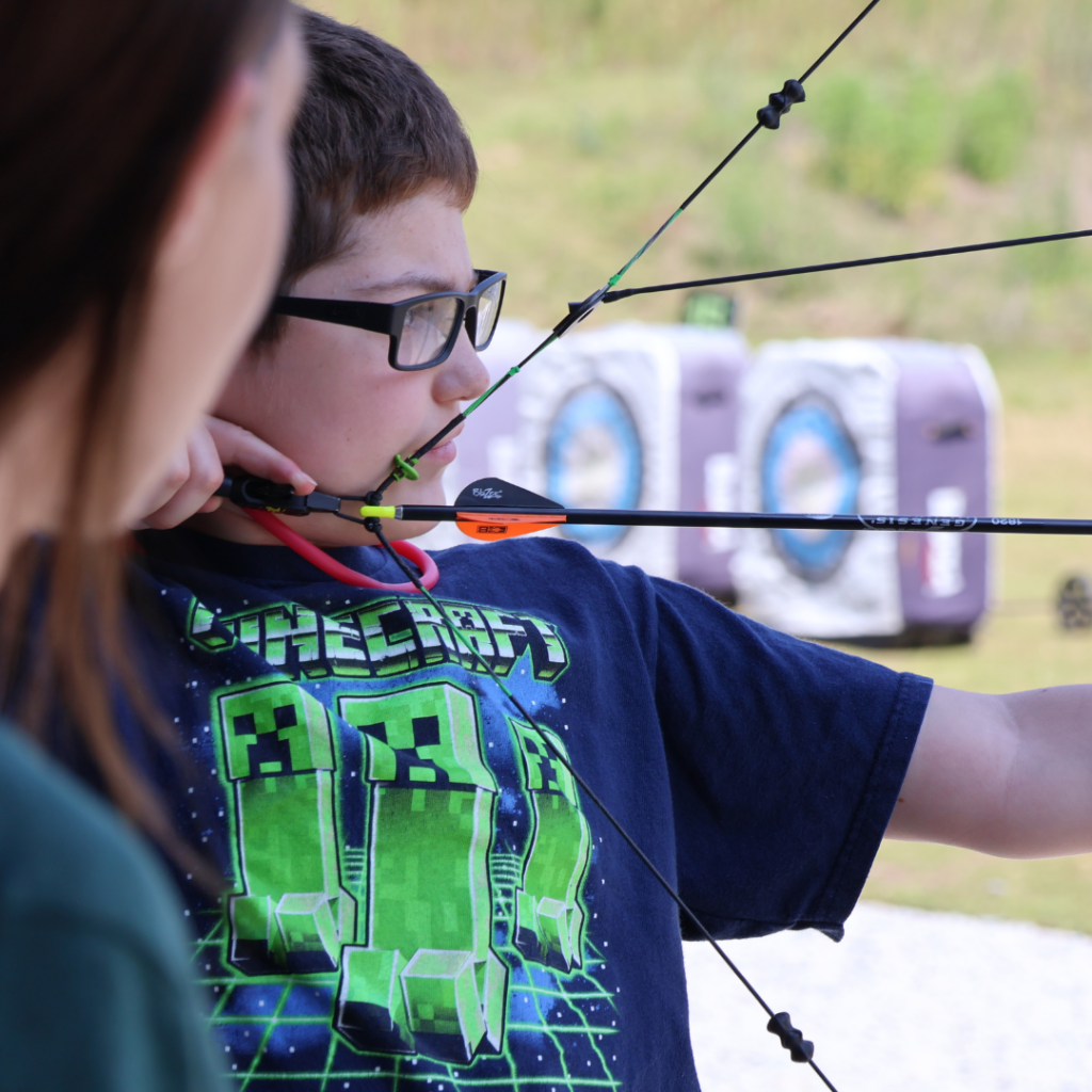 A young boy taking aim with a bow and arrow at The Quiver Archery Range