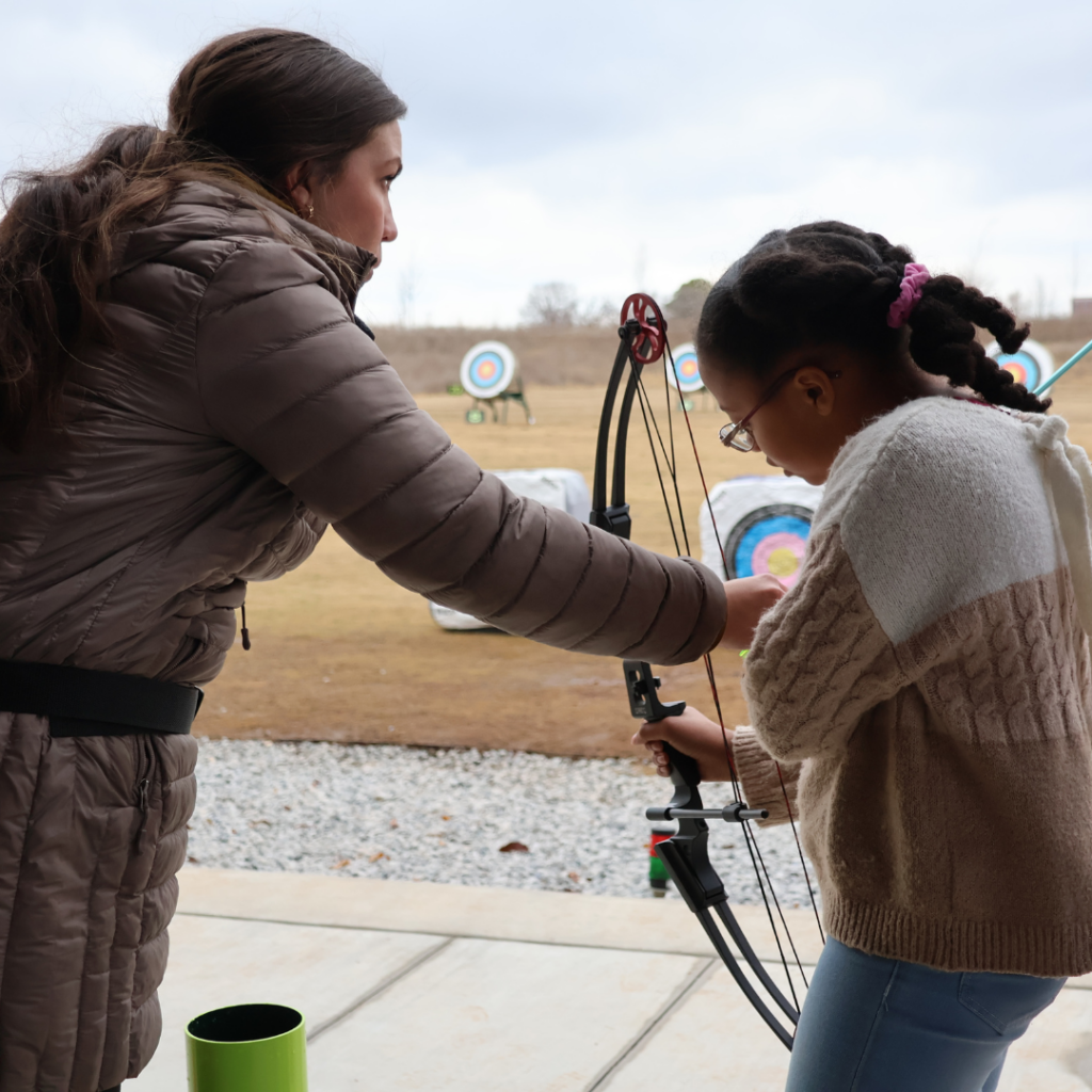 Whitney, Kids Camp Instructor, teaching a child to shoot her first arrow at a target