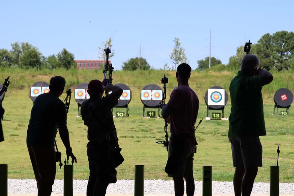 Silhouettes of 4 archers standing in front of archery range targets in bentonville, arkansas