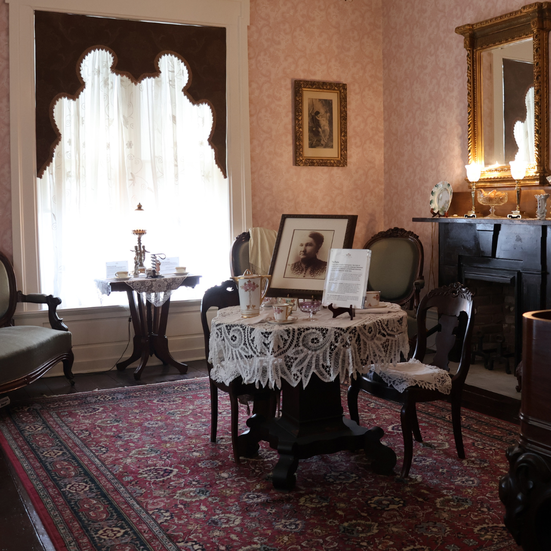 The Parlor at Peel Museum (a round table with a doily over it featuring a photo of Mary Emaline Peel)